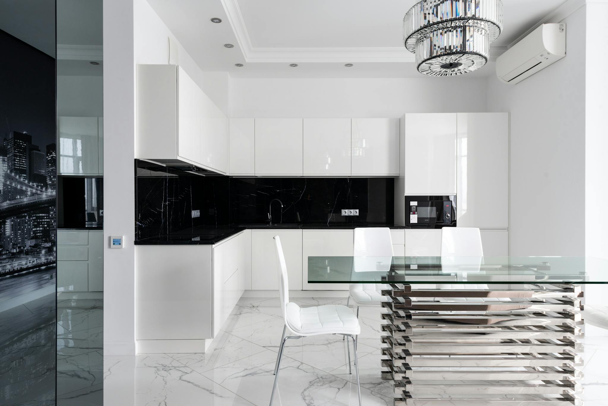 Interior of light modern studio with glass table near chairs under chandelier next to open kitchen with white cabinets